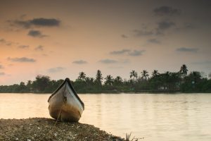 Traditional fishing boat on the riverbank at sunset in Betul village, Goa, India, with palm trees and tranquil water creating a peaceful tropical landscape.